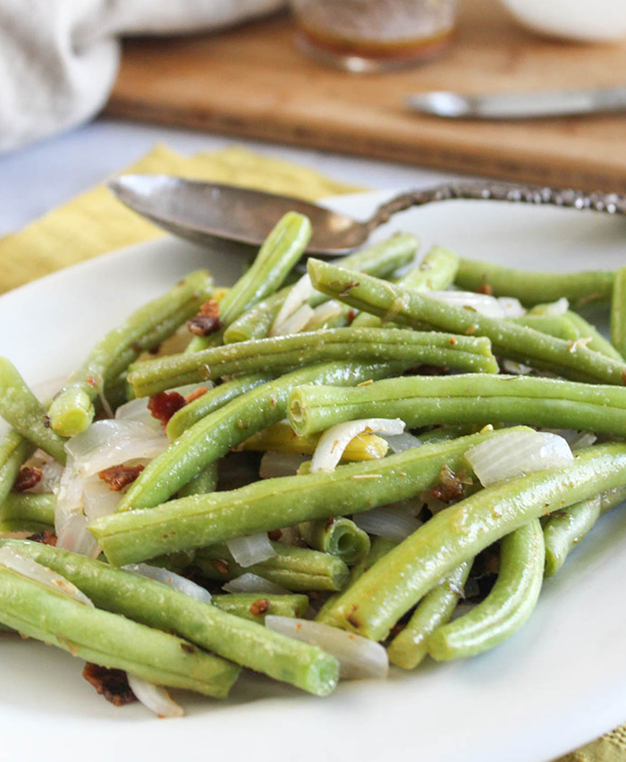 Green beans and onions with bacon on a white plate