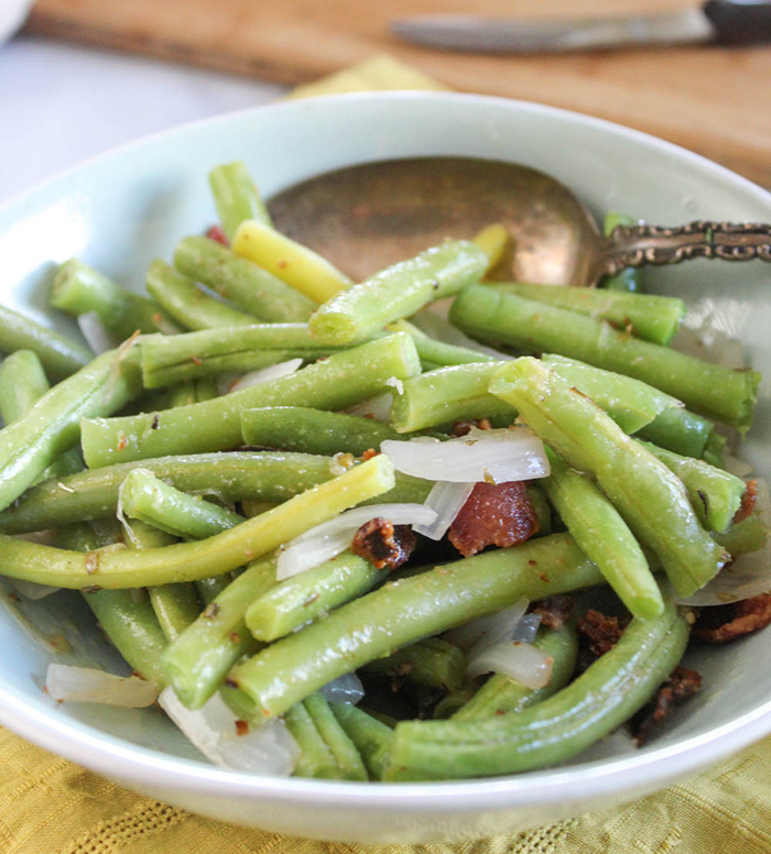 a close up of green beans with bacon and onions in a bowl