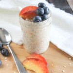 a close up picture of overnight oats in a jar topped with blueberries and peaches