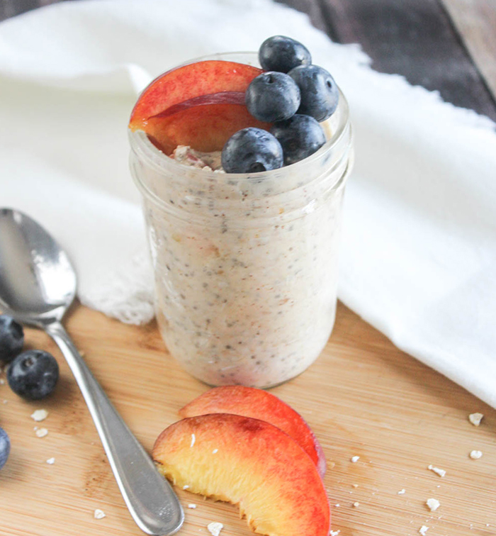 a close up picture of overnight oats in a jar topped with blueberries and peaches