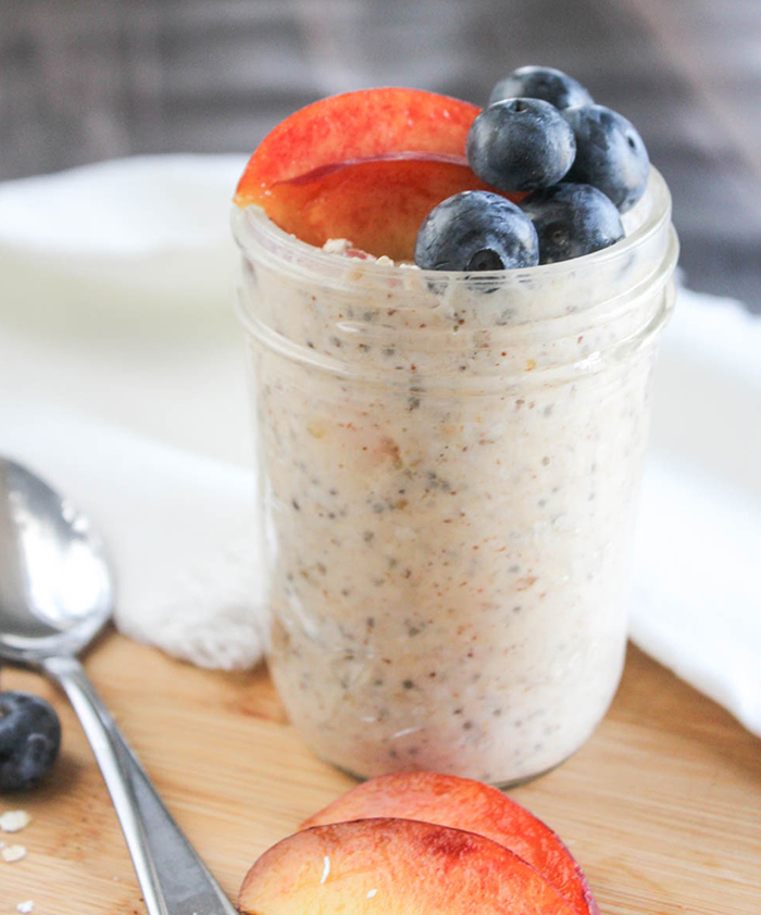 a close up picture of peach overnight oats in a jar topped with blueberries and peaches