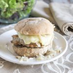 turkey burger on a roll with sauerkraut and melting cheese on a white plate