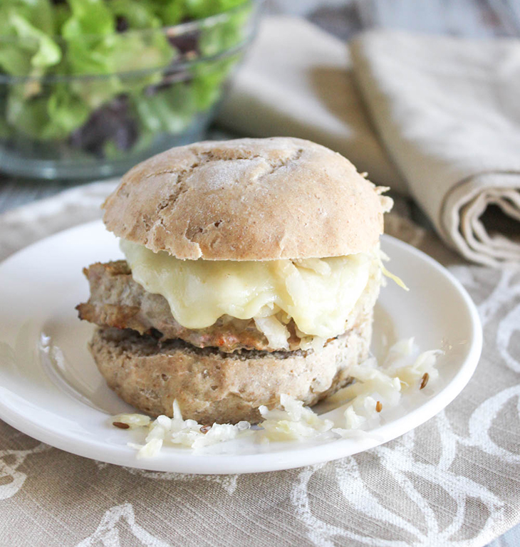 a turkey burger on a roll on a white plate with a bowl of salad in the background