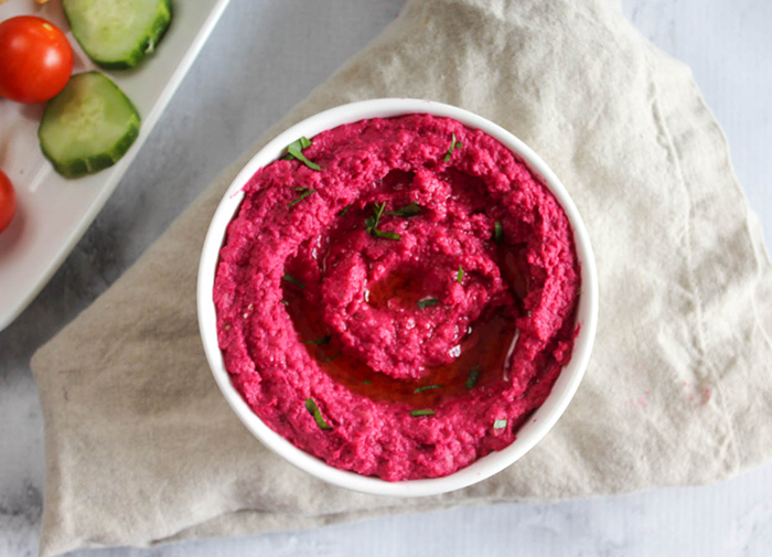 a view looking down at a bowl of pink beet hummus with oil and parsley on top