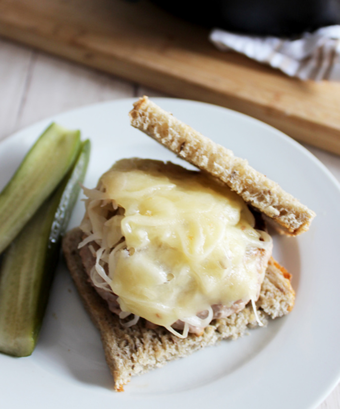 Turkey burger topped with sauerkraut and melted swiss cheese on rye bread with a pickle on the side.