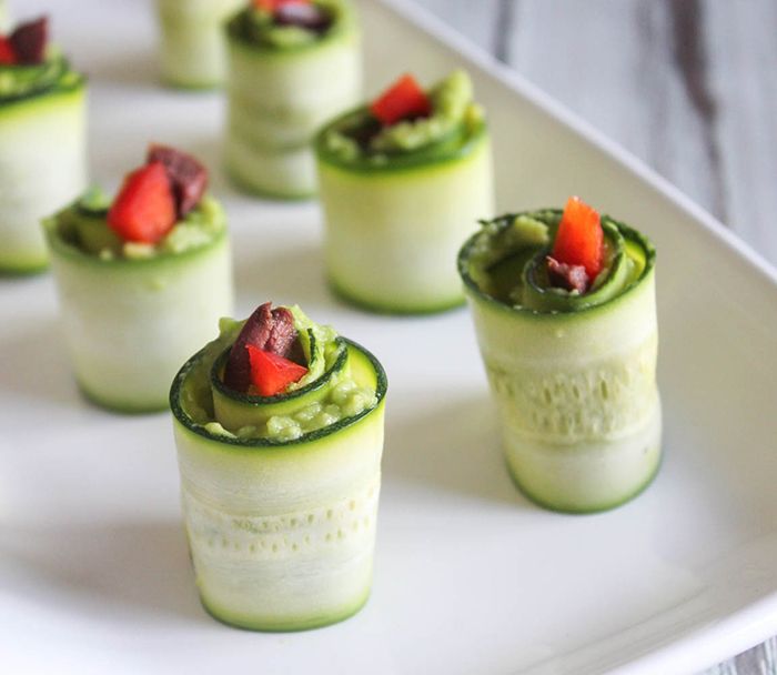 zucchini rolls topped with peppers and olives on a white plate