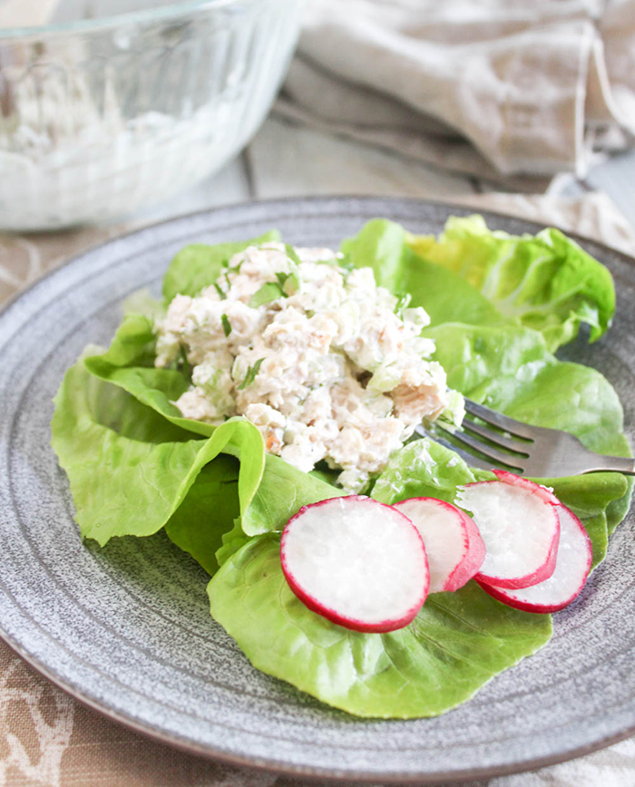 A close up of chicken salad on lettuce with raddish slices on a plate with a fork