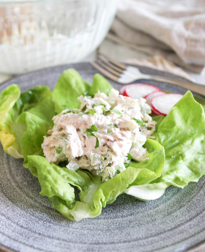 a close up of chicken salad on a top of lettuce on a plate with a fork on the side 