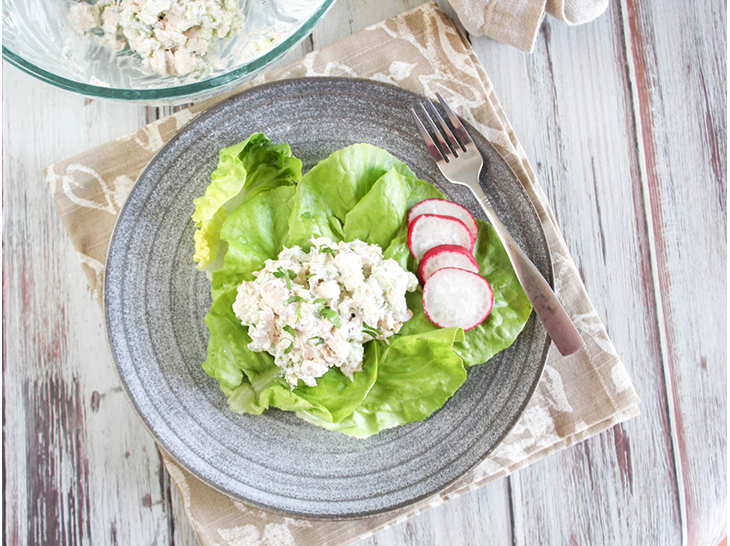 An overhead view of chicken salad on letuce with radish slices and a fork