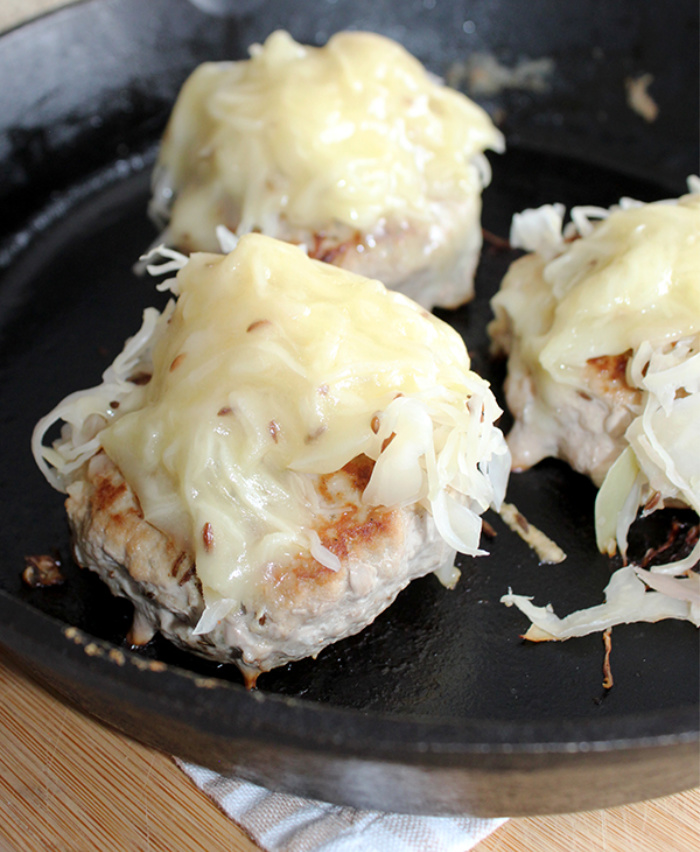 cooked turkey burgers in a cast iron pan sauerkraut and cheese on top 