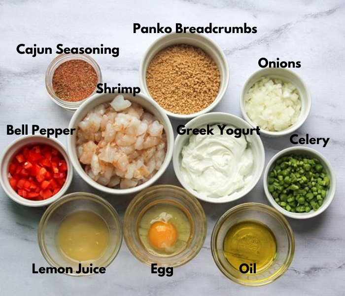 overhead view of ingredients in bowls to make spicy shrimp cakes including shrimp, bell pepper, cajun seasoning, onions, celery, greek yogurt, celery, panko breadcrumbs, lemon juice, egg, oil