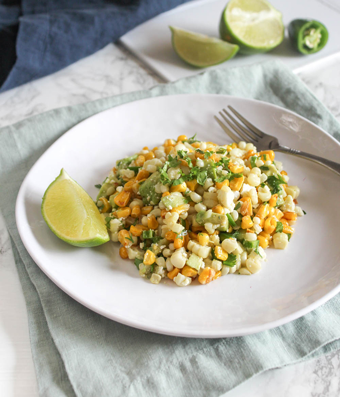 A plate full of mexican corn salad with a fork and slice of lime