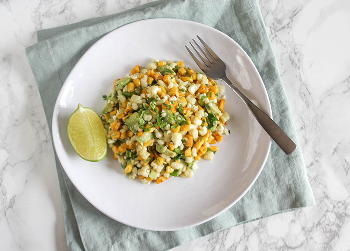 an overhead shot of corn salad on a white plate with a fork