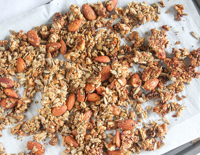 This picture is step five in the recipe. The baked granola is golden and crispy and is still on the parchment-lined baking sheet.