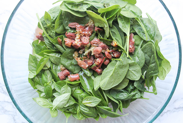 a picture of spinach basil salad in a bowl with prosciutto on top