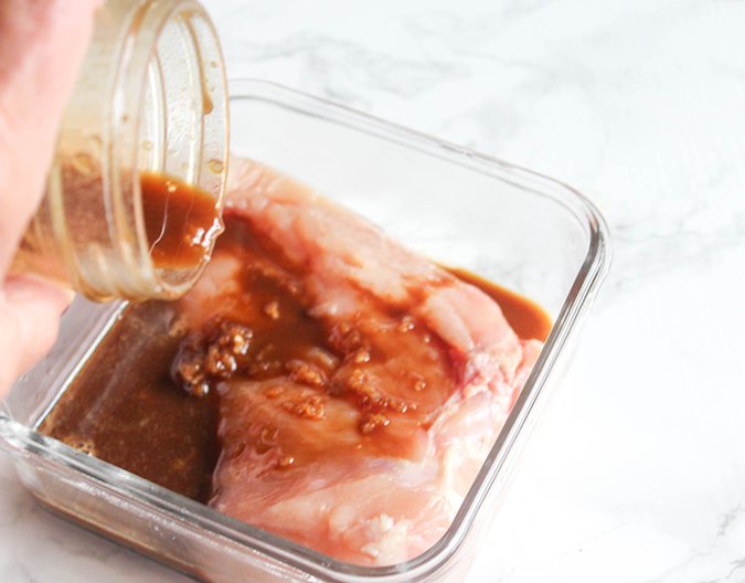 Pouring marinade over the chicken. Chicken is in glass baking dish.