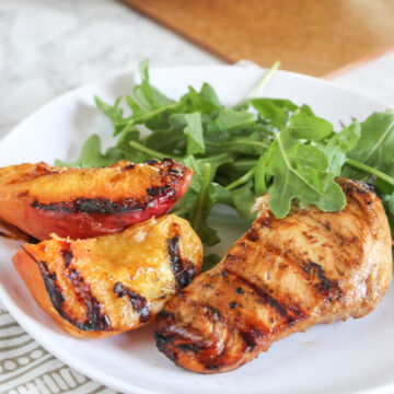 a plate of grilled chicken and peaches with salad