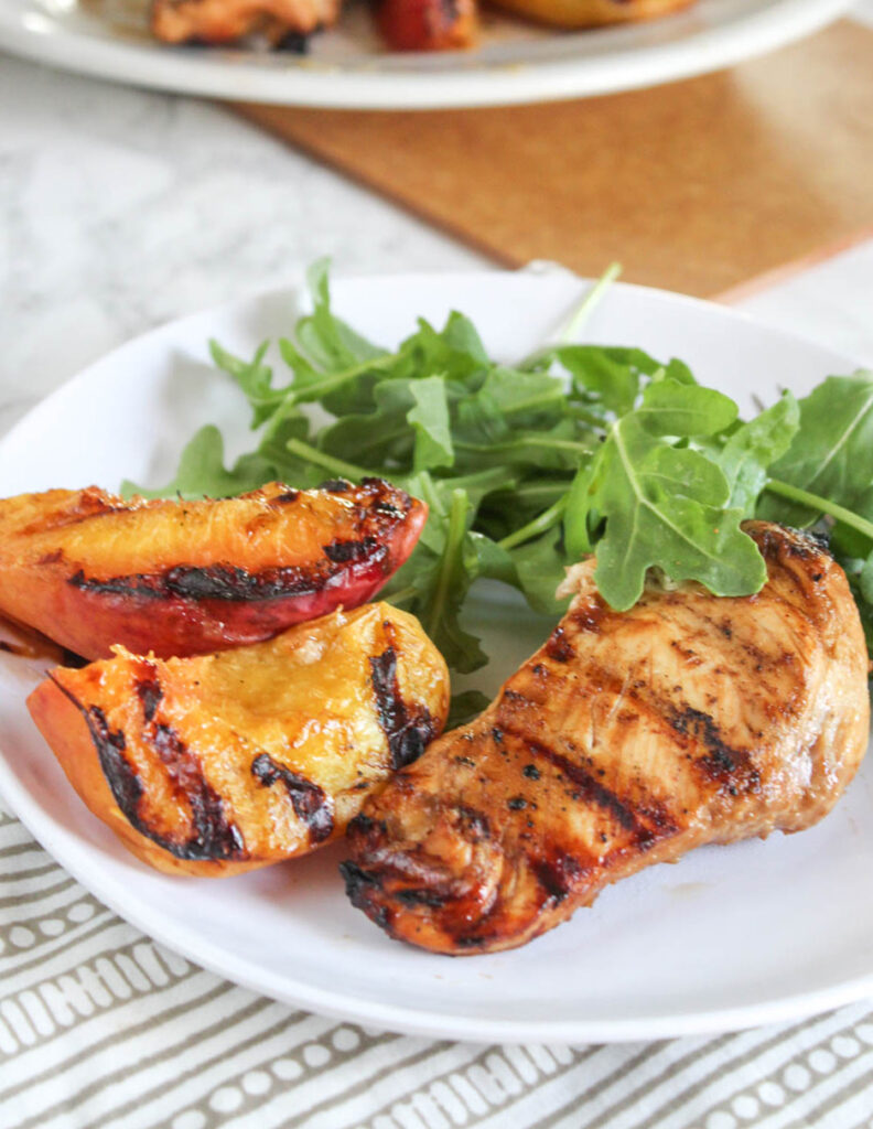 Grilled peaches and chicken on a plate with arugula