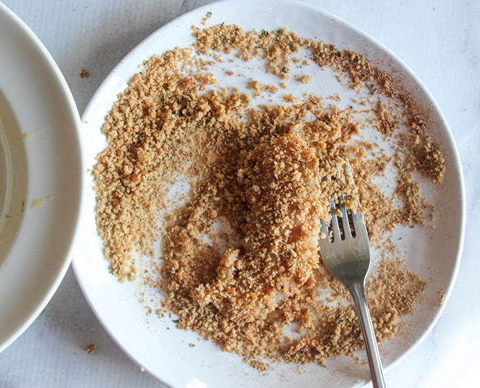 chicken tender on a plate covered with breadcrumbs