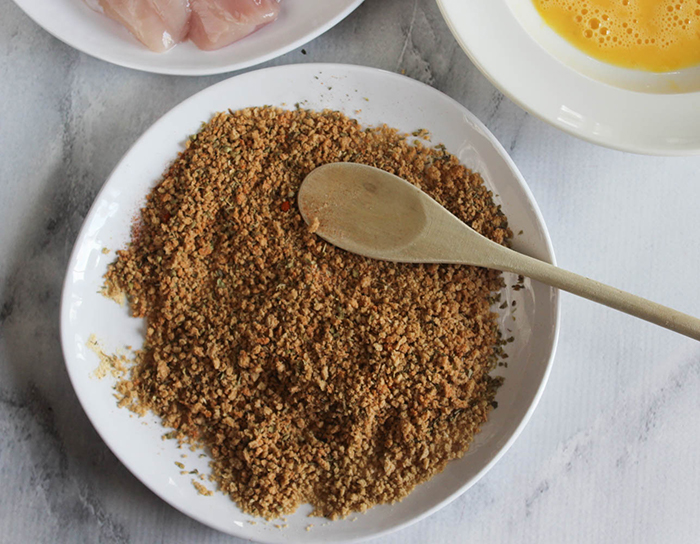 a picture of bread crumbs on a white plate with a wooden spoon