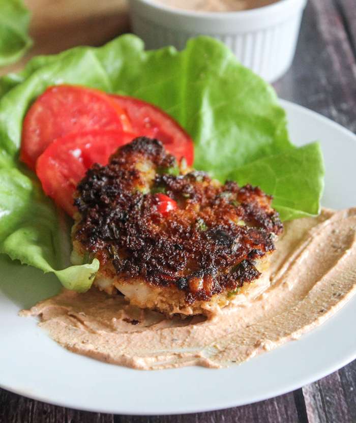 A close up picture of a shrimp cake cooked on a plate with lettuce and tomatoes