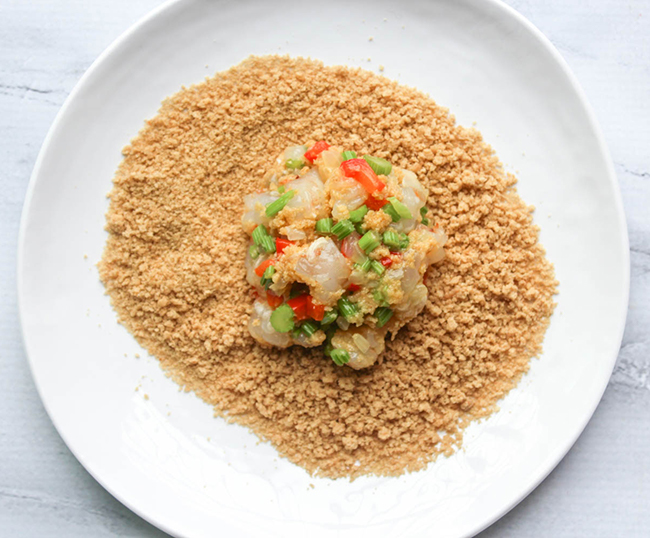 a picture of shrimp cake being dipped into bread crumbs