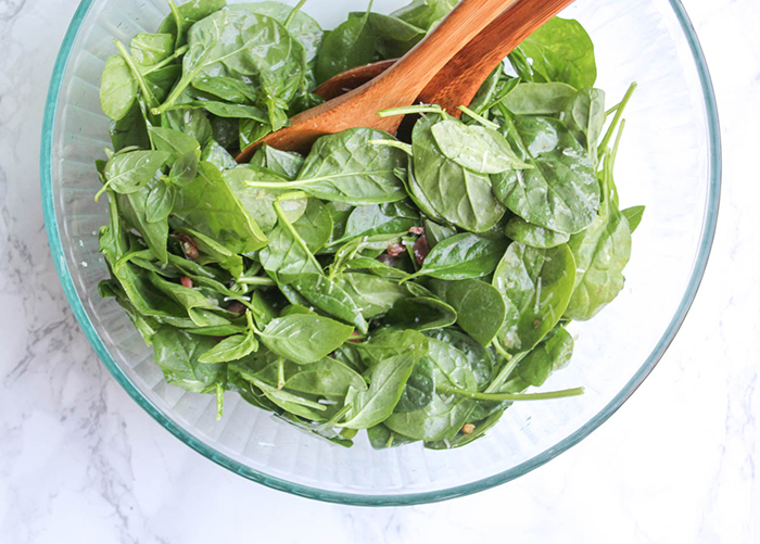 an overhead view of the mixed up salad in a glass bowl with wooden spoons