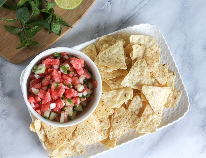 a view looking down at the watermelon salsa in a white bowl with a tray of chips