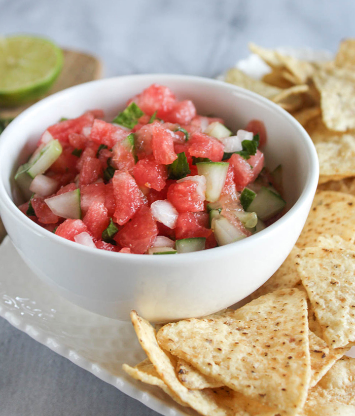 watermelon and cucumber salsa in a white bowl surrounded by chips