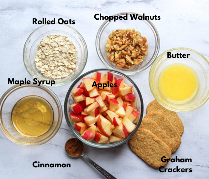 The ingredients for apple crisp in bowls: rolled oats, chopped walnuts, melted butter, maple syrup, apples, cinnamon, graham crackers