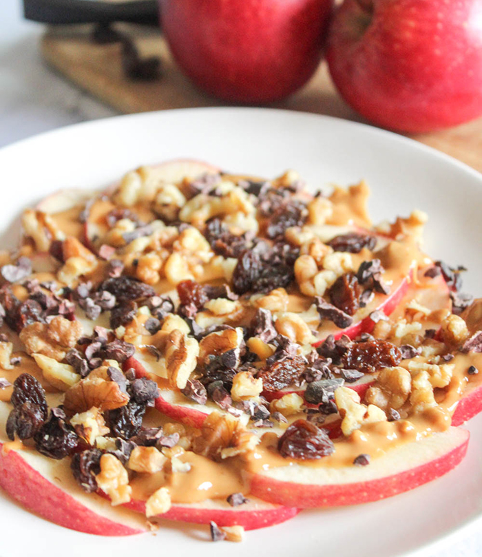 A close up picture of apple slices topped with walnuts, peanut butter and raisins