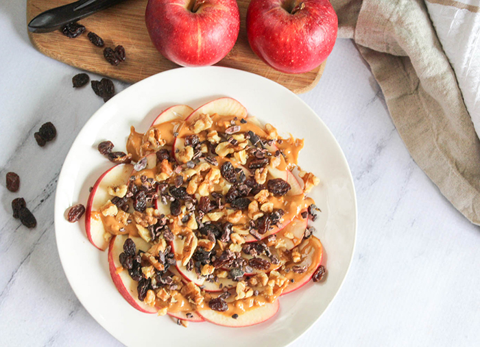 An overhead view of apples, peanut butter raisins and walnuts on a plate
