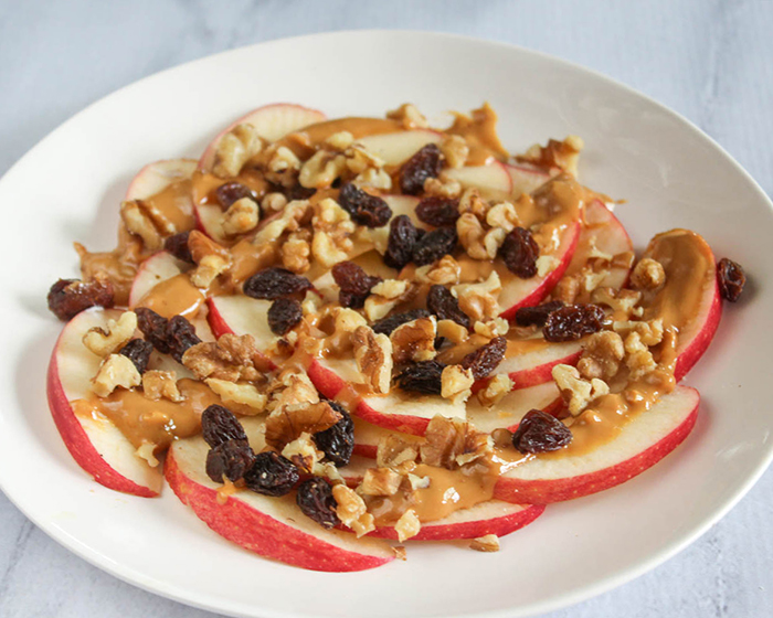 sliced apples with peanut butter, walnuts and raisins on top of them