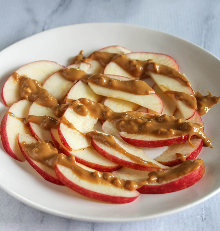 apple slices with a drizzle of peanut butter on a white plate