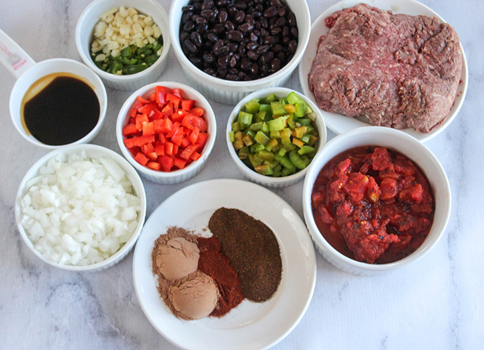 These are ingredients in the picture to make bison chili in white bowls and one measuring cup holding the brewed coffee. Ingredients pictured are: ground bison, black beans, garlic, onion, bell peppers, jalapeno pepper, chipolte chili powder, chili powder and crushed tomatoes. 