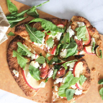 an overhead of a cooked flatbread with figs, apples, goat cheese and arugula cut into 4 pieces