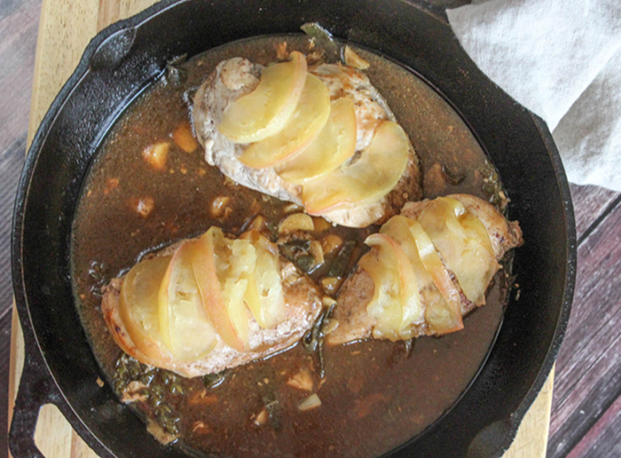 chicken topped with baked apple slices in a pan