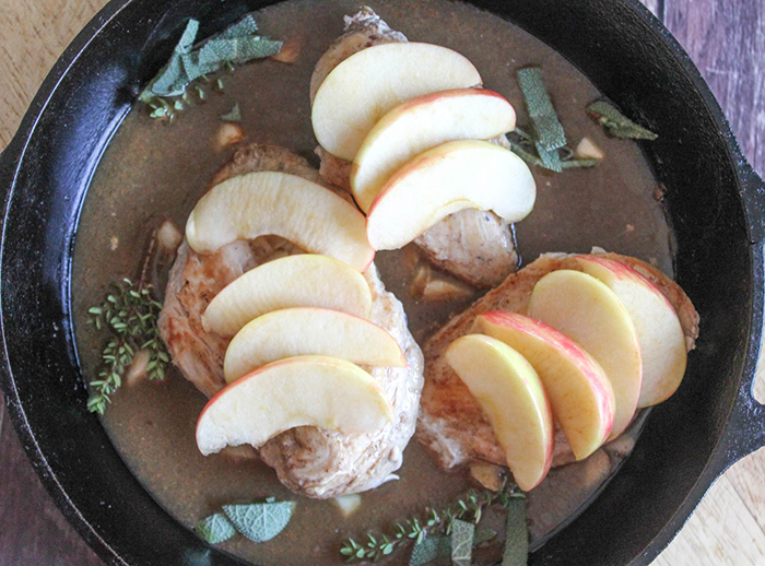 Chicken in a skillet with a brown sauce sage and apples