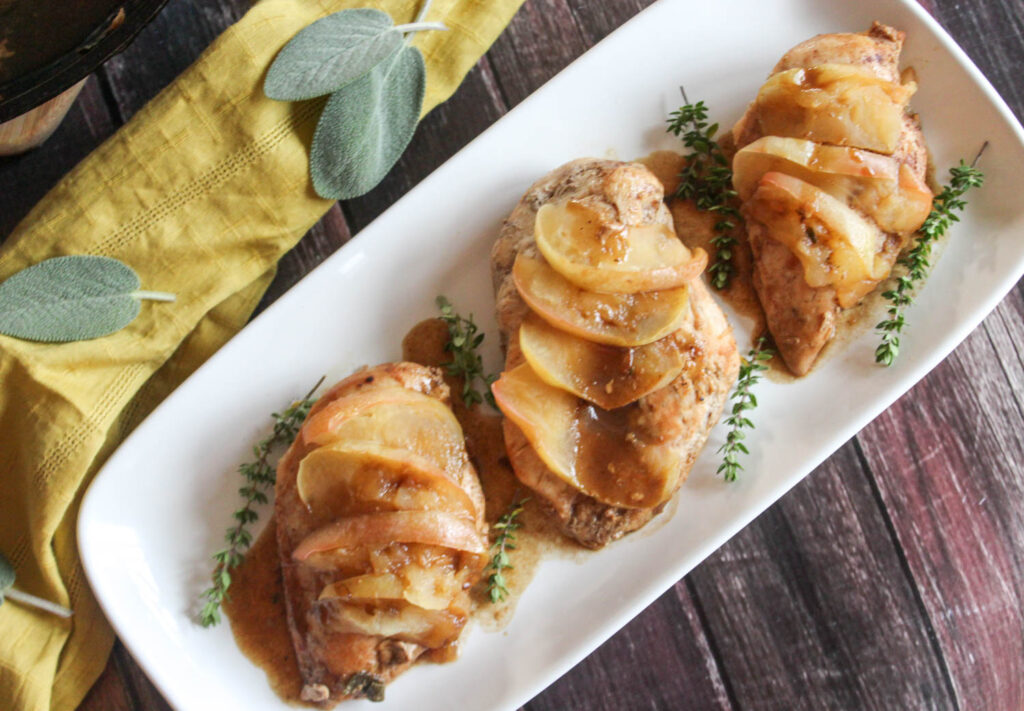 an overhead view of the finished recipe, three boneless chicken breasts with slices of apples and thyme