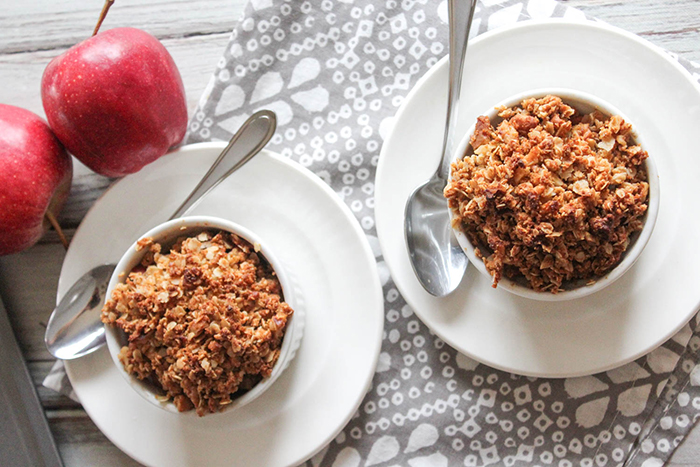 an overhead view of two portions of apple crisp in two separate white ramekins on a white plate