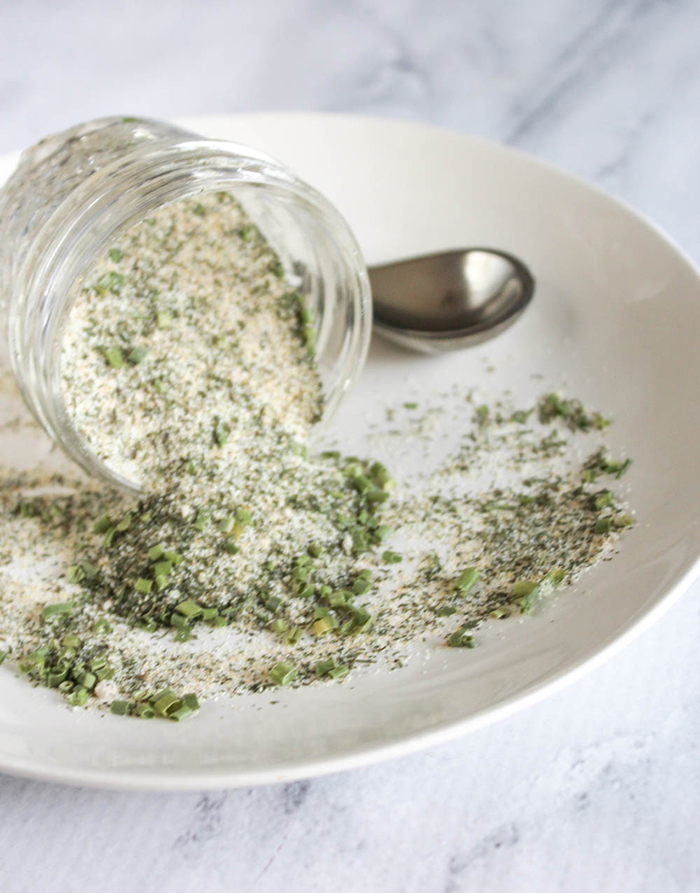 ranch spice blend spilling out of a glass jar onto a plate with a spoon in the background