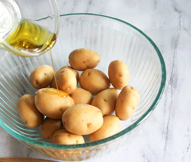 baby potatoes in a bowl with oil pouring on them