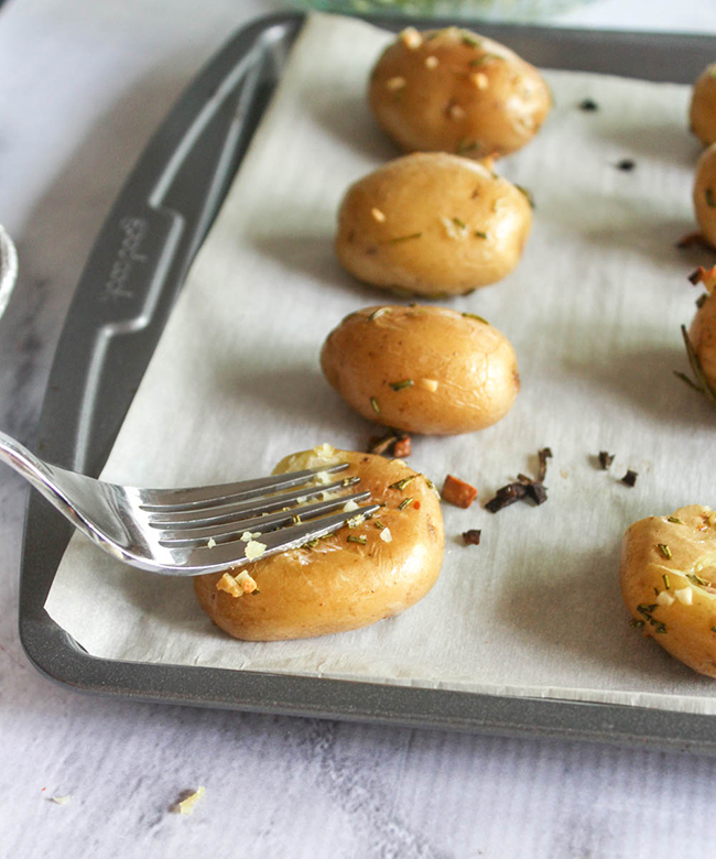 A fork smashin a potato on a baking sheet