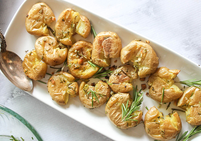 an overhead view of smashed potatoes on a palte with fresh rosemary