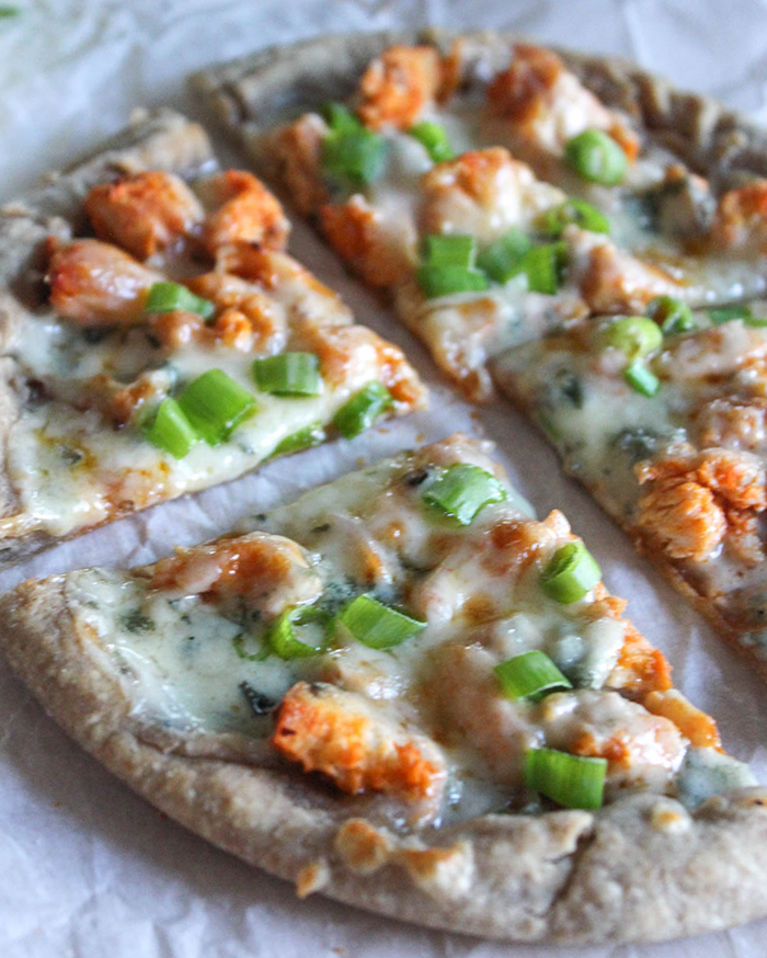buffalo chicken flatbread pizza on white parchment paper with melted cheese and green onions