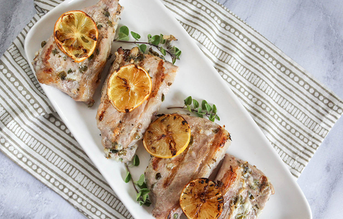 an overhead view of boneless pork chops with lemons and oregano on a white platter