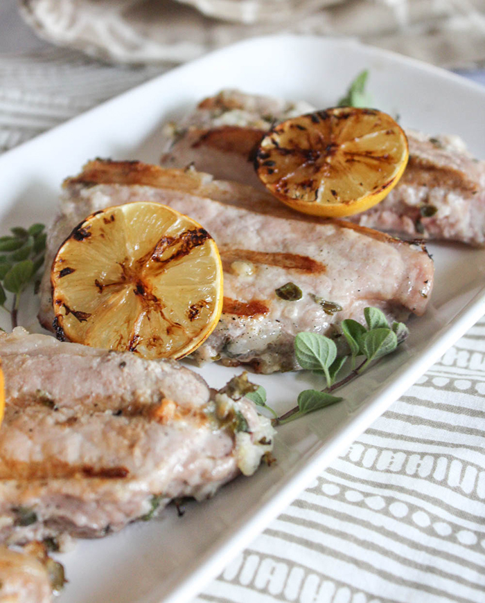 Mediterranean grilled pork chops on a platter with grilled lemons