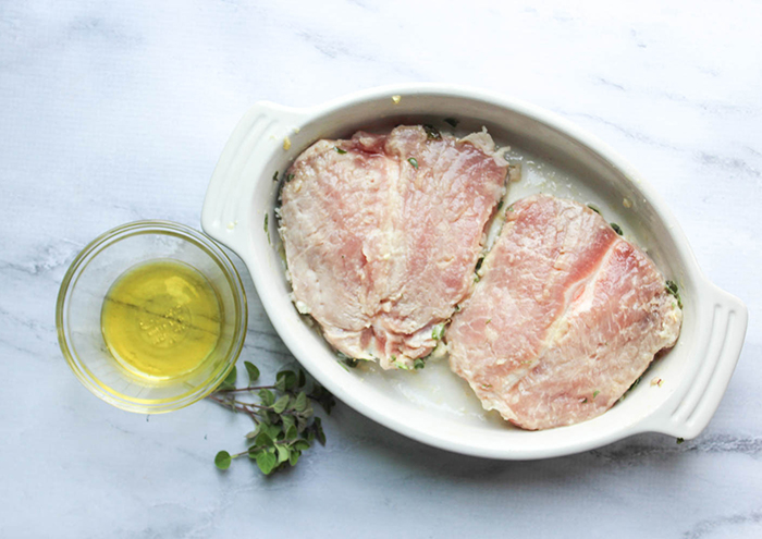 The ingredients: boneless pork chops in a white bowl, olive oil and oregano