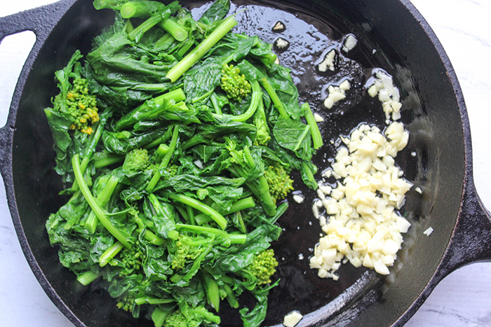 an overhead view of broccoli rabe and chopped garlic in a skillet