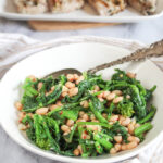a close up picture of sauteed broccoli rabe in a white bowl with a serving spoon